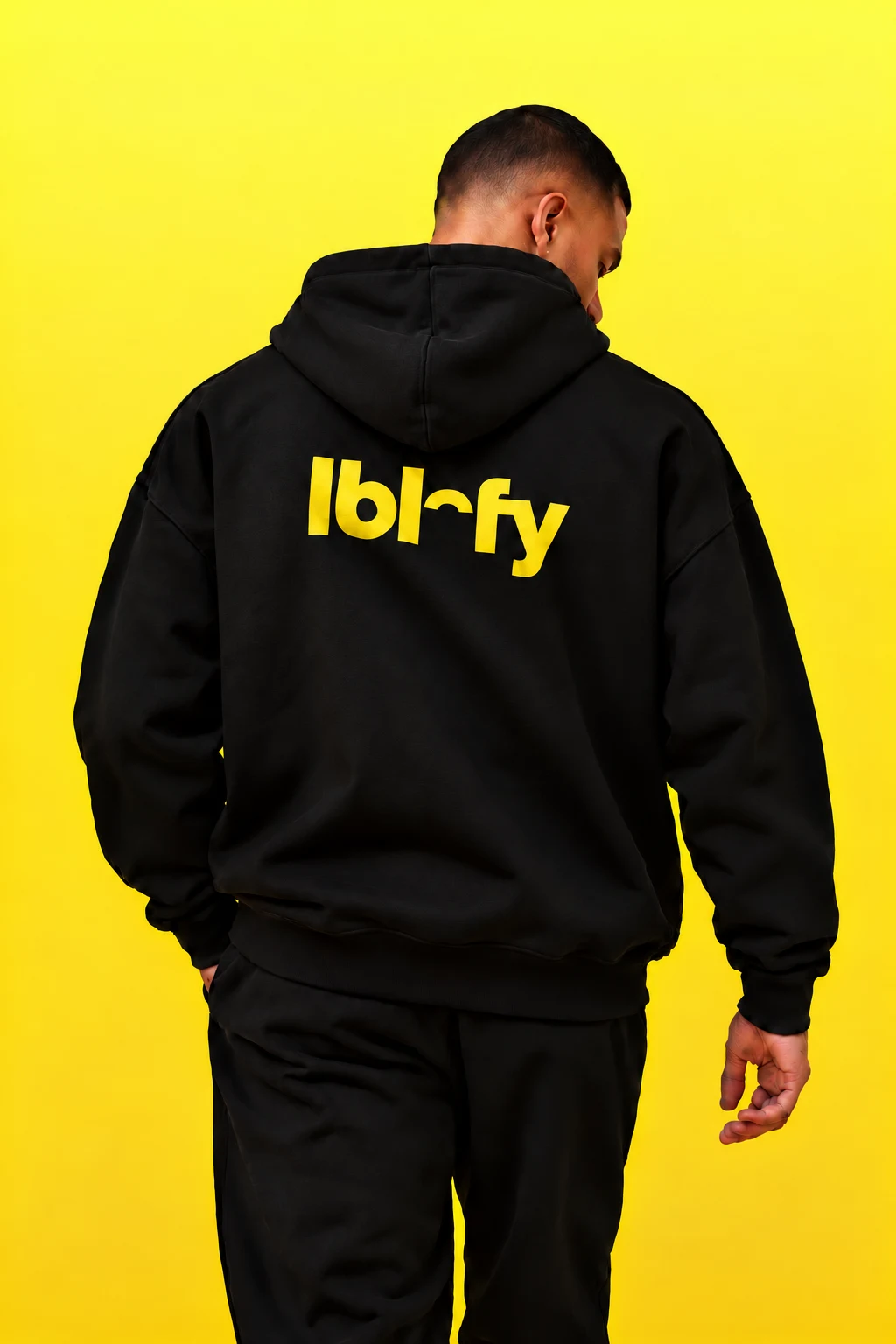 Back view of a black hoodie against a yellow background